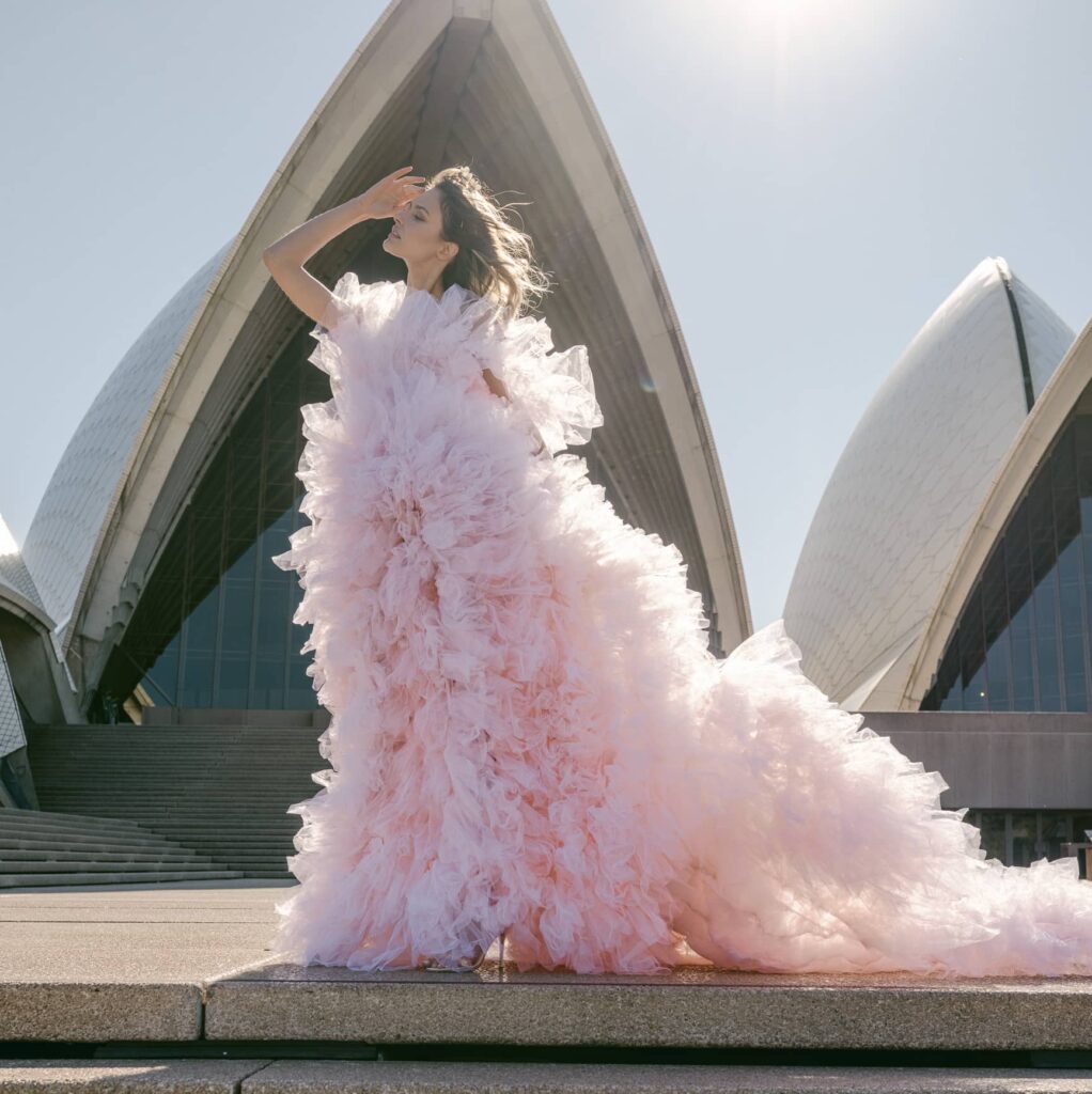 Bride is standing in front of the Sydney Opera House in blush couture wedding gown 